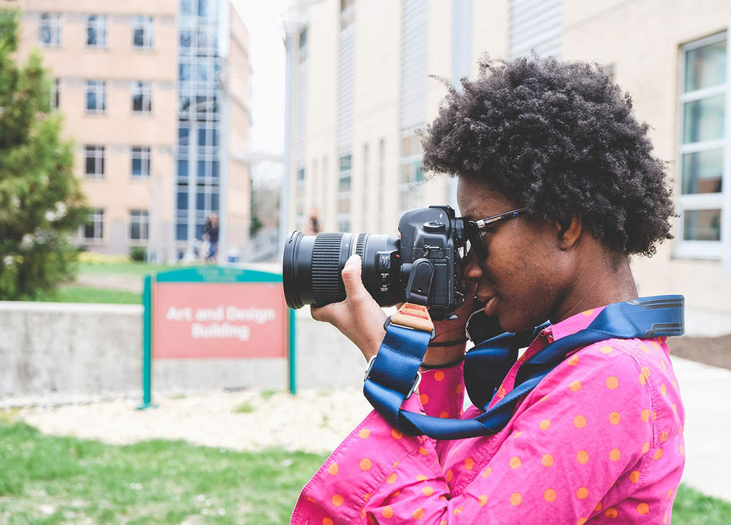 African American woman taking photos with camera outside Art and Design building