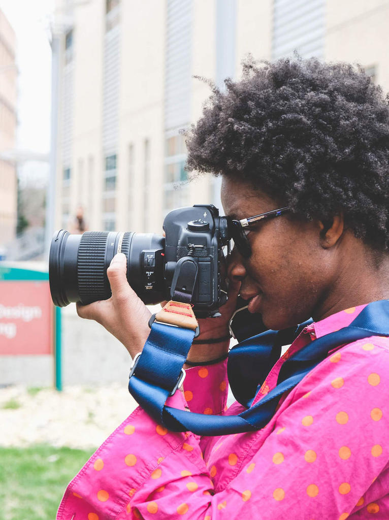 African-American female standing sideways looking through lens of camera