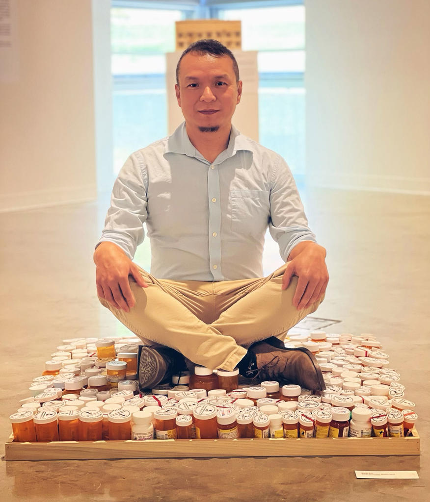 Steven Luu sitting on pill bottles being part of his exhibition 'Reinventing My Narrative'